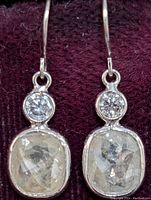 Front view of both earrings on maroon fabric background showing bezel-set cushion rose cut diamonds and round brilliant accents