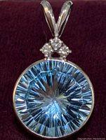 Close-up front view of the pendant showing the round blue topaz center stone and diamond accents above it.