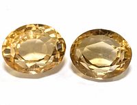 Two oval faceted citrine gemstones shown close up on white background, exhibit yellow-orange translucent color.