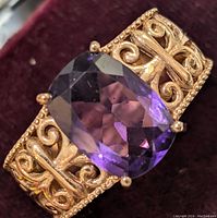 Close-up photo showing the large faceted amethyst set in an ornate sterling silver band with scroll and knot pattern detail.