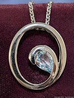 Close-up front view of the silver pendant with blue topaz on a maroon background.