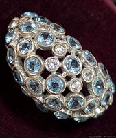 Close-up image of sterling silver ring showing multiple round blue topaz stones bezel-set along with smaller round white stones in a dome/openwork style setting on velvet background.