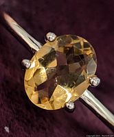 Close-up of the oval faceted citrine gemstone set in sterling silver ring band with four prongs.
