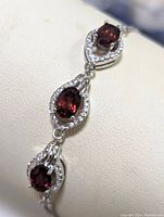Close-up view of bracelet detail showing oval garnet stones surrounded by cubic zirconia in sterling silver settings.