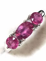 Three-stone top-angle close-up showing larger center oval ruby with two smaller rubies on each side.