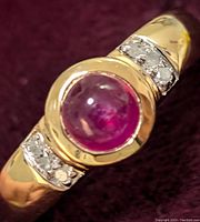 Close-up image of the sterling silver ring showing the round cabochon ruby center stone and white topaz accents on either side.