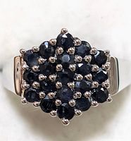 Close-up front view of sterling silver ring with multiple faceted blue sapphires in cluster setting on broad band.