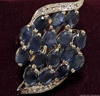 Close-up of sapphire ring showing oval blue stones in cluster with white stone accents on curved silver edges