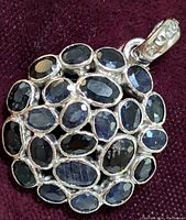 Close-up front view of the round sterling silver pendant with multiple oval-shaped blue sapphires set in cluster pattern on dark fabric background.