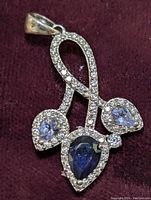 Front view of the sterling silver pendant showing pear-shaped sapphire and tanzanite stones with clear stone accents on a maroon fabric background.