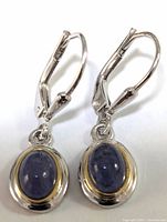 Pair of sterling silver drop earrings with oval cabochon tanzanite stones, showing the lever-back clasps and two-tone bezel setting.