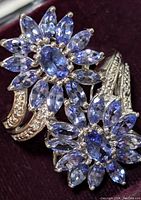 Close up image of the silver ring with flower-shaped tanzanite clusters and clear stones on the band, showing detailed design and stone clarity.