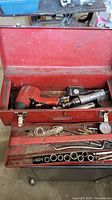 Open red toolbox showing air impact wrench, air ratchet wrench with gauge, sockets, dial gauge, hand tools and cords