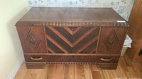 View of the closed antique mahogany cedar chest showing the lid and front decorative wood inlay with a latch on top.