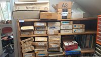Cardboard boxes on shelves labeled with electronic parts names such as servos, leads, resistors, switches, relay, regulators, and other RC aircraft electronic components.