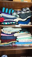 Assorted folded fabric pieces stacked in two shelves, showing various colors and patterns such as stripes, plaid, and solids.