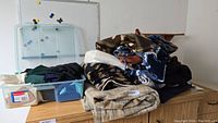 Photo showing folded assorted fleece and knit fabric including camouflage, patterned blue and white, black abstract print, tan plaid.