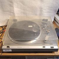 Top view of Hitachi HT-324 turntable fully covered with a scuffed clear dust cover and control buttons on front panel.