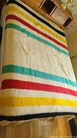 Full view of blanket on bed showing cream background with navy, yellow, red and green stripes.