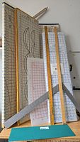 Front view of folding pattern cutting boards with grid lines and pattern shapes, yard stick, meter stick, and metal square.
