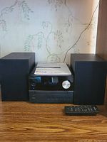 Front view of Pioneer X-EM26 micro chain CD receiver system with two black speakers on each side and remote control on wooden surface.