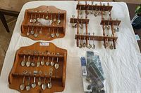 Full view of three wooden display racks holding approximately 35 souvenir spoons with varied designs spread across multiple rows on a white cloth background.