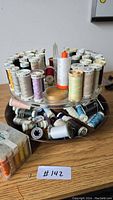 Thread caddy filled with multiple spools of thread of various colors and brands on a wooden surface.
