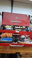 Photo of open red toolbox showing various tools including orange-handled screwdrivers and multiple tools scattered inside.