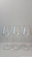 Photo of three identical clear plastic wine glasses with long stems and round bases, arranged side by side against a plain background.