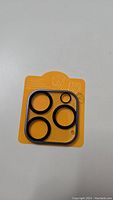 Photo of black camera lens protector rings of different sizes and a square frame, arranged on a yellow backing card.