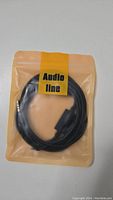 Photo of a black audio cable coiled and sealed in clear plastic with yellow 'Audio Line' label.