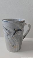 Front view of tall marbled gray and white ceramic mug with gold Libra constellation and Libra text.
