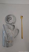 Side view of ceramic mug with marbled gray and white finish, gold constellation, and gold spoon beside it