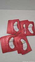 Photo shows multiple individually packaged pink sachets containing the crescent-shaped white gel under eye pads, laid out on a flat surface.