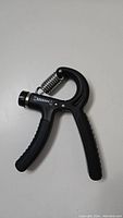 Black hand grip strengthener with ergonomic handles and tension adjustment knob.