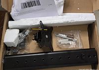 Photo of monitor stand parts including the metal arm, mounting plate, tempered glass base and hardware bags in packaging.