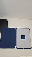 Blue tablet cover opened flat showing soft gray interior lining and tri-fold front cover