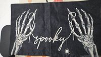 Black pillow cover with skeletal hands and the word 'spooky' with a spider below the text.