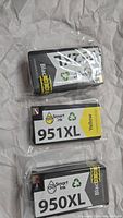 Photo of three printer ink cartridges wrapped in plastic, showing HP 950XL black and 951XL yellow cartridges with Smart Ink branding.