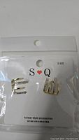 Photo showing two silver-tone earrings on an S Q branded card inside a sealed plastic bag.