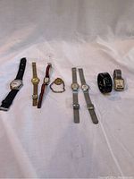 Full lot of 8 vintage watches arranged in a line on a white cloth background showing a variety of band materials and colors.