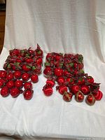 Photo showing large 2.5-inch plastic red apple ornaments along with red satin ball ornaments, all tied with plaid ribbons or bows, displayed against white background.