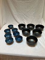 Set of blue glazed bowls and brown glazed rice bowls arranged on a white cloth background.