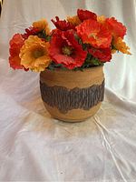 Tan ceramic pot with dark brown textured bark band filled with a colorful silk Iceland poppy bouquet in reds, orange, and yellow, shown from front angle.