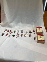 Wide shot of all 18 Christmas Krinkles ornaments arranged in a row with two original boxes to the right, showing scale, variety, and packaging