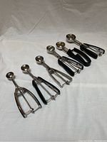 Six cookie scoops of different sizes arranged on a light fabric background, showing side view and handle design.