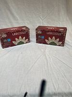 Two unopened red boxes of Santas Forest LED C6 faceted clear bulb string lights, 50 bulbs each.