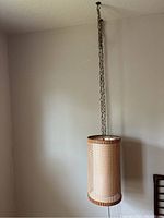 Full view of MCM hanging lamp suspended from ceiling, showing cylindrical shape with mesh outer and fabric inner shade.
