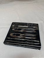 Top view of crab forks and nut crackers arranged in the molded slots of a black plastic case on a white background.