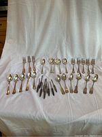 Overview of all flatware items laid on a white cloth; includes forks, spoons, and nut picks.